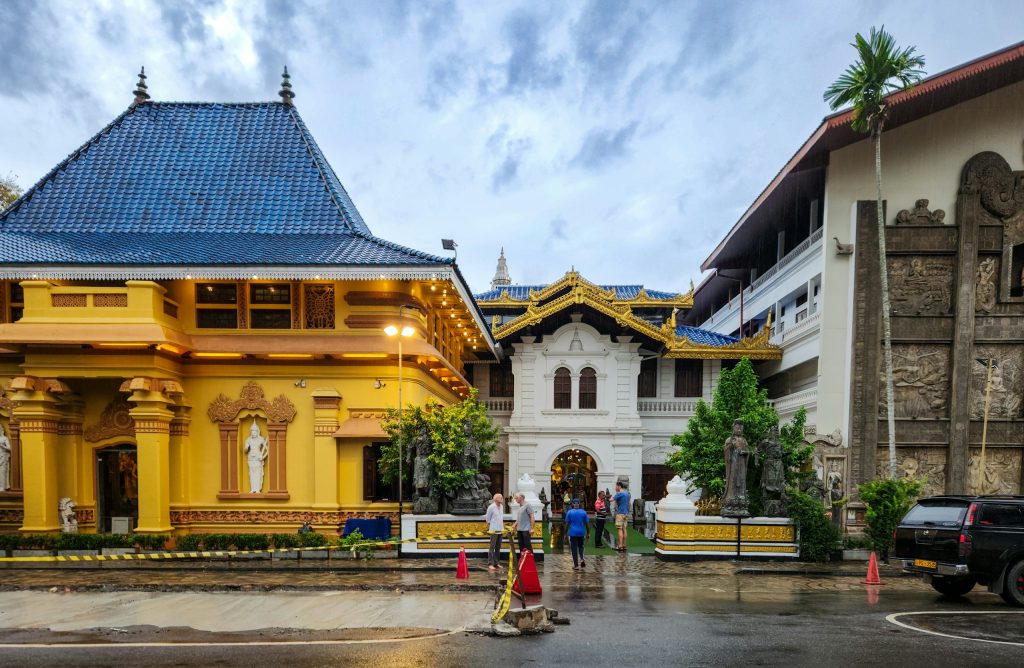 Yellow shrine with a blue tiled roof beside a white arched gateway at Gangaramaya Temple, Colombo