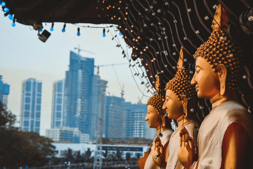 Row of golden Buddha statues at Gangaramaya Temple, with Colombo's high-rise skyline behind