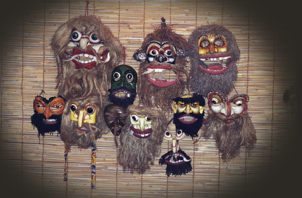 A wall of painted wooden demon masks with bulging eyes, bared teeth and long fibre beards