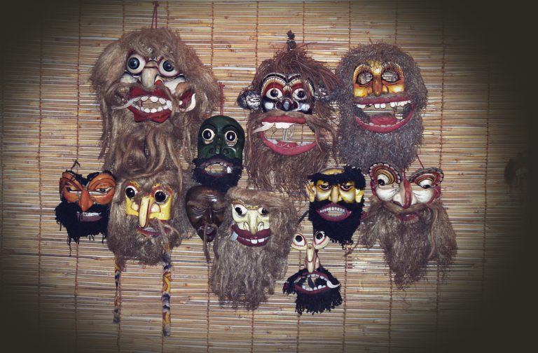 A wall of painted wooden demon masks with bulging eyes, bared teeth and long fibre beards