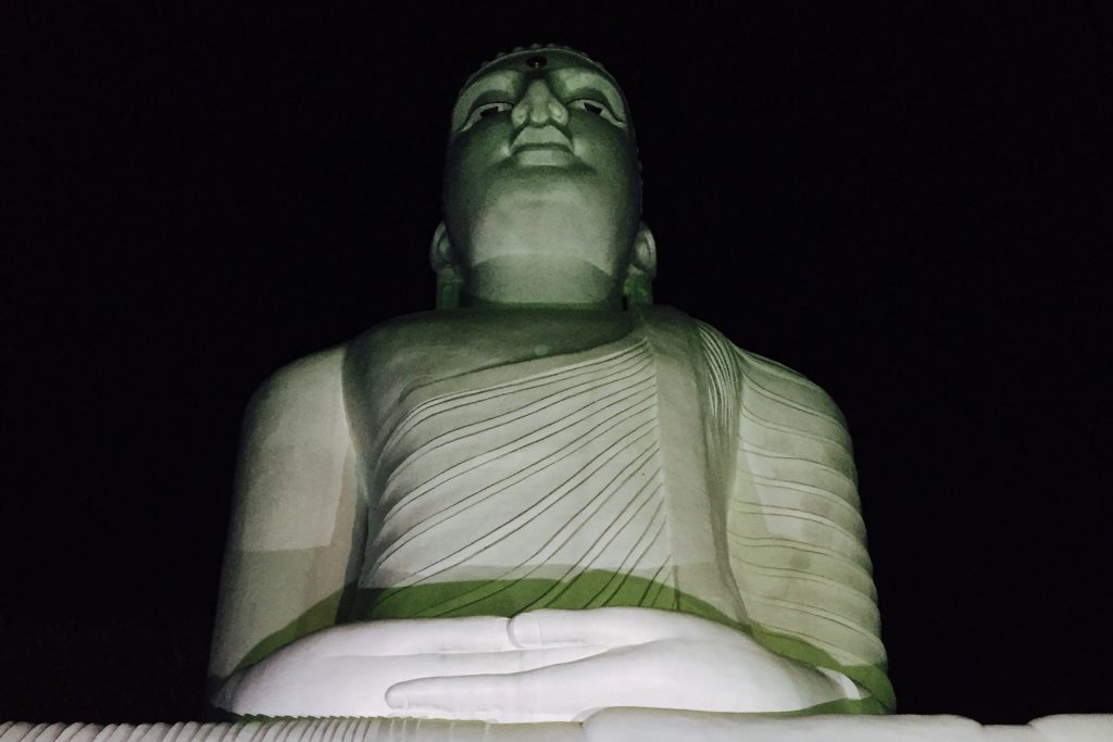 The large white seated Buddha statue at Bahirawakanda lit at night, seen from below with its hands in its lap