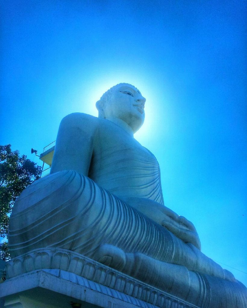 The seated Buddha statue seen from the side against a blue sky, with its hands resting in its lap