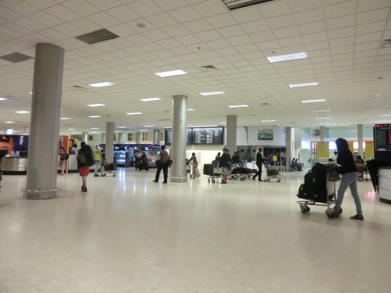 Travellers with luggage trolleys in the arrivals concourse at Bandaranaike International Airport, with a Mobitel counter and flight information screens behind