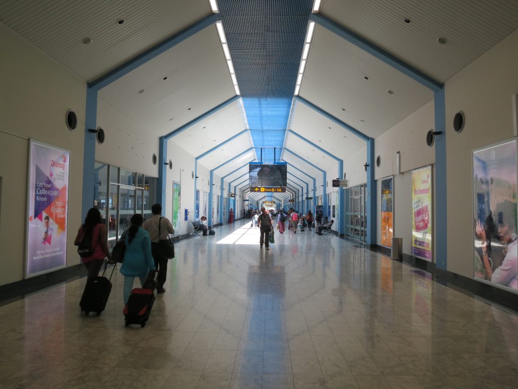 Passengers with wheeled suitcases walking along a long, bright corridor past the gate signs at Bandaranaike International Airport
