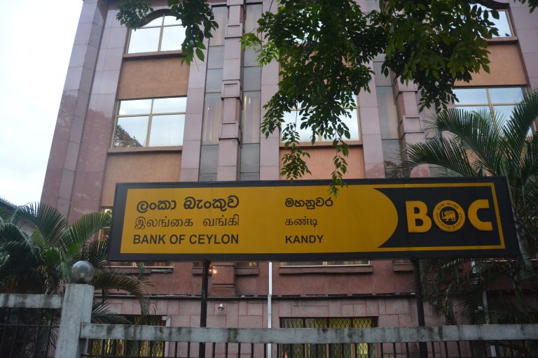 Yellow Bank of Ceylon sign reading Kandy in Sinhala, Tamil and English in front of the bank's stone-clad branch building