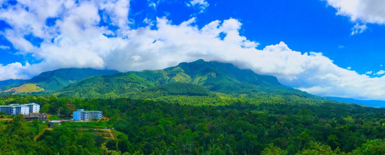 Forested hills and a cloud-capped mountain above Belihuloya, with Sabaragamuwa University buildings among the trees in the foreground