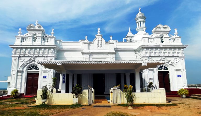 The white Kechimalai Mosque in Beruwala, with ornate gables, arched wooden doors and a domed minaret under a blue sky
