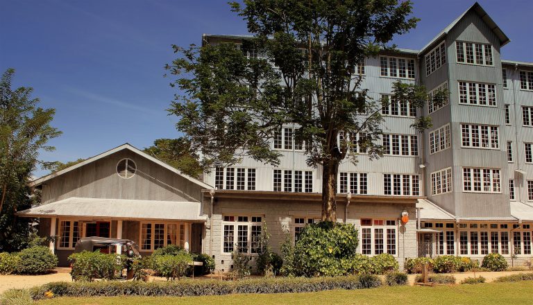 The grey-clad, multi-storey former tea factory that houses the Ceylon Tea Museum, with a tree and garden in front