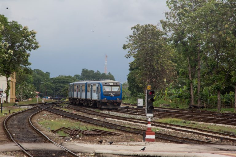 A blue diesel train approaching Colombo Fort railway station past a signal, with several tracks in the foreground