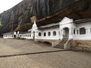 The white arched fronts of the Dambulla cave shrines under a huge overhanging rock