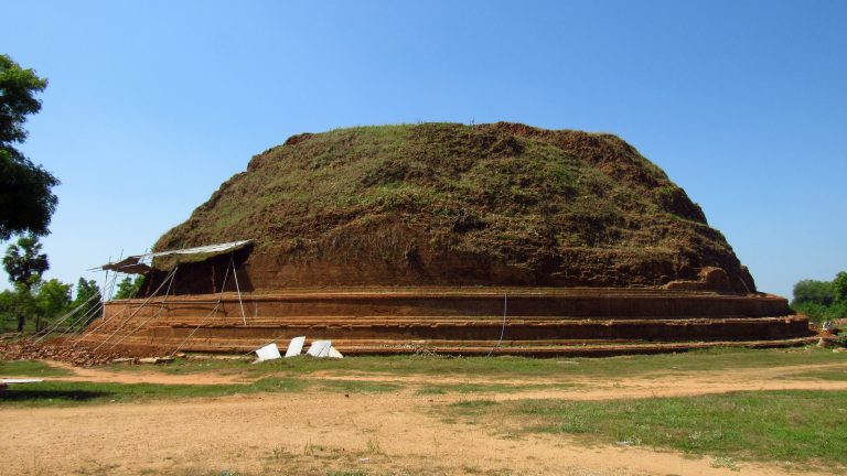 The ruined brick stupa at Deegavapi, a broad grass-covered mound above stepped brick terraces, under a clear blue sky