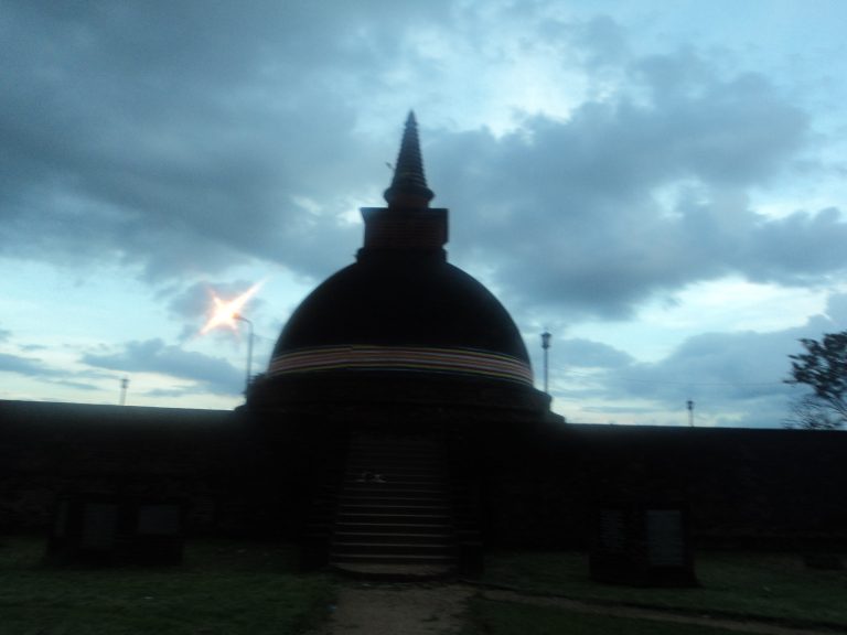 Dematamal Viharaya's dark stupa and whitewashed image house surrounded by trees at Okkampitiya