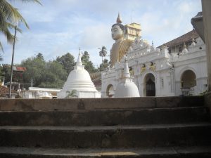 The white temple gateway and two small stupas at Wewurukannala Vihara, with the head and shoulders of the giant seated Buddha rising behind