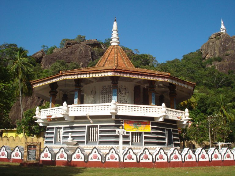The ornate pavilion-style shrine of Dimbulagala Raja Maha Vihara at the foot of the rock, with a small white dagoba visible on the summit behind it