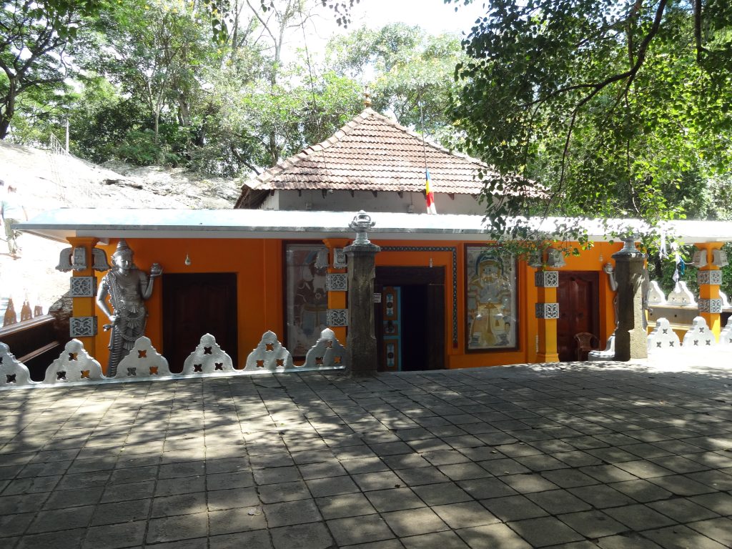 The orange front of the cave image house at Dowa under a tiled roof, with a carved guardian figure on the left and painted panels beside the doorway