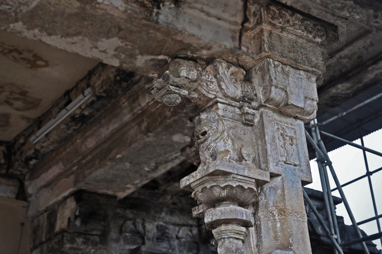 Close-up of a carved stone pillar at Gadaladeniya, with a lotus-shaped capital, an animal-head bracket and a relief figure in a square panel
