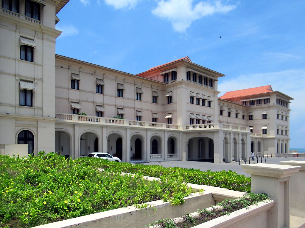 The cream colonnaded front and red-tiled roofs of the Galle Face Hotel on a sunny day, with a planted terrace in the foreground