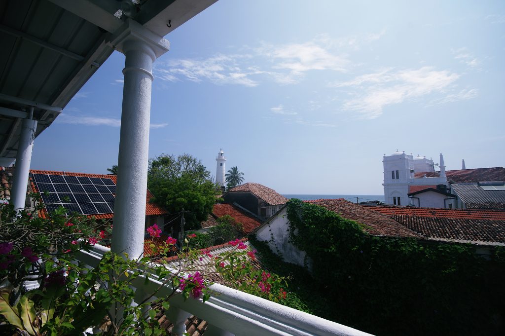 Red-tiled roofs inside Galle Fort under a blue sky, with the white lighthouse and the Meeran Jumma Mosque in the background