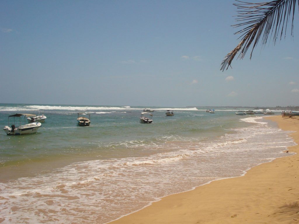 Boats sitting in the shallows off Hikkaduwa beach with waves breaking on the reef beyond