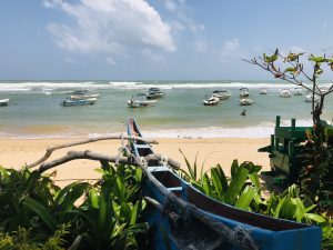 Glass-bottom boats moored in the shallow reef lagoon at Hikkaduwa, seen from the beach past a wooden fishing boat