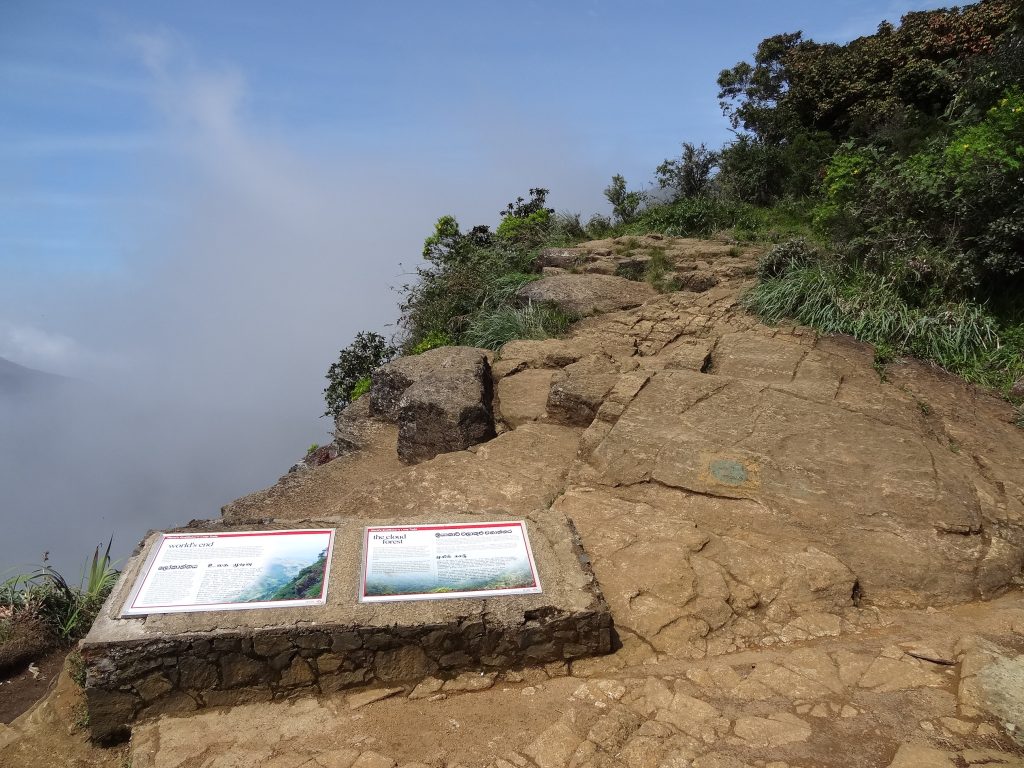 Rocky path and information boards at the World's End viewpoint, with cloud filling the valley beyond the edge