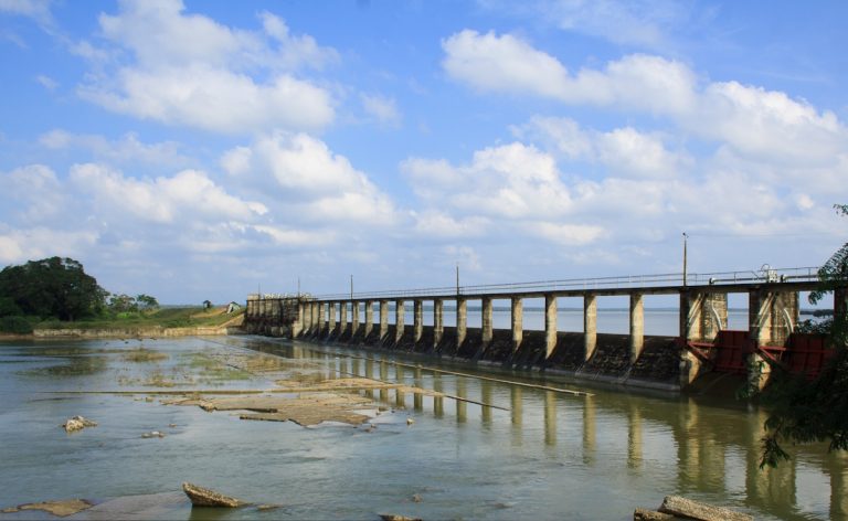 Iranamadu Tank's long concrete spillway and row of sluice gates stretching across the reservoir, with paddy land beyond