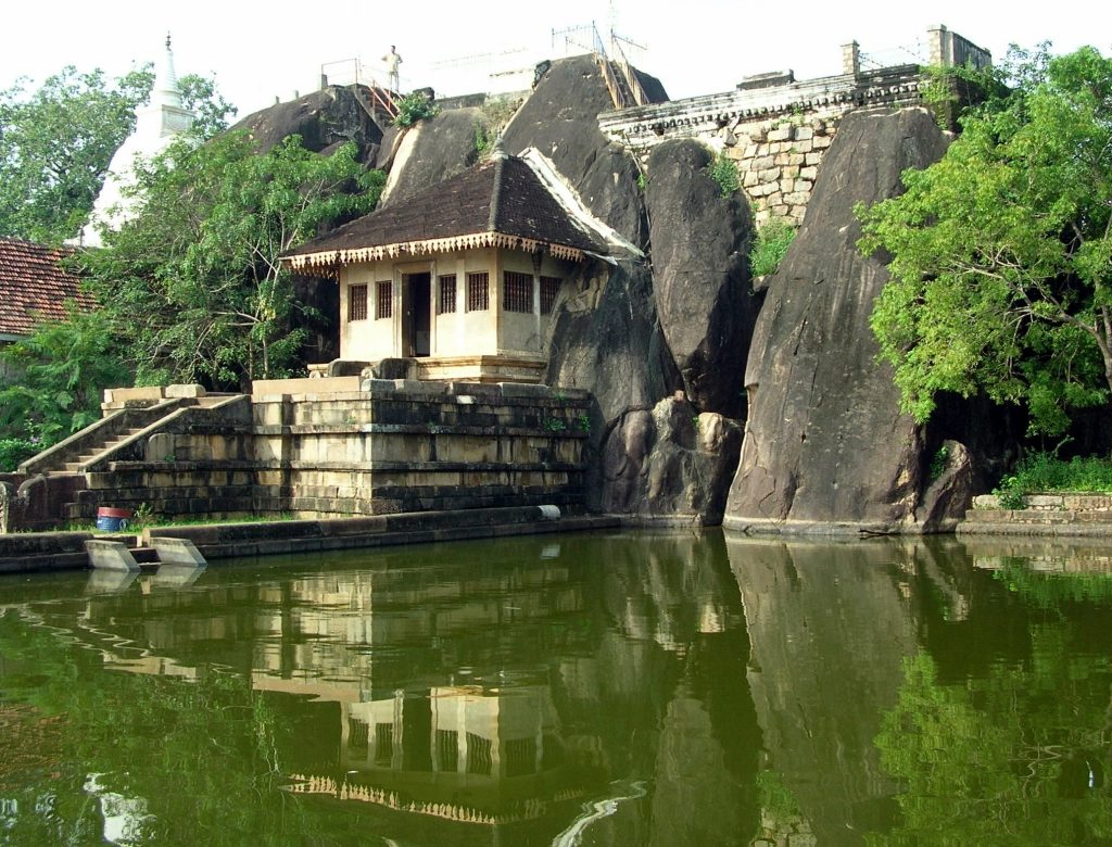 The Isurumuniya pond reflecting the rock shrine and granite boulders, with an elephant carved in the rock just above the waterline