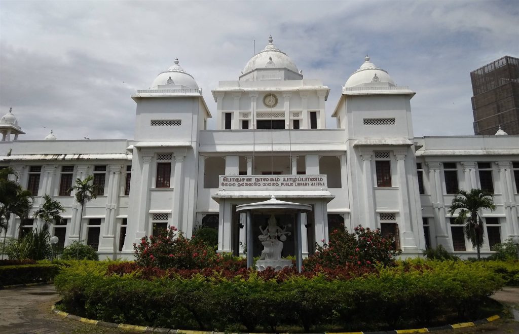 The white three-domed facade of the Jaffna Public Library with its name in Tamil, Sinhala and English and a statue of Saraswati in the forecourt