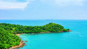 A small sandy cove backed by thick forest, with turquoise water and a wooded point of land running out into the sea