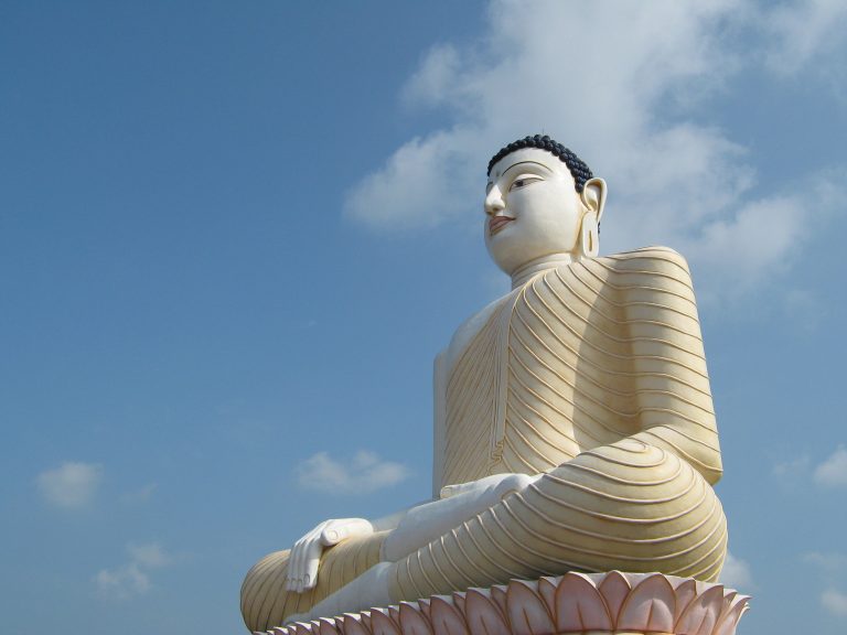 The giant seated Buddha statue at Kande Vihara on its lotus pedestal, seen from below against a blue sky