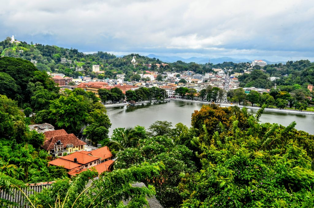 Kandy Lake and the town around it seen from a wooded hillside, with hills and a white Buddha statue on the skyline