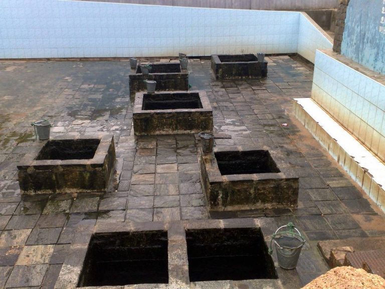 Square stone-lined wells set in a paved floor with metal buckets beside them
