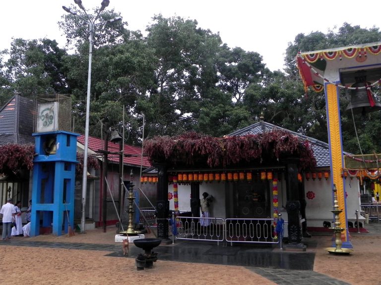 The garlanded Maha Devale shrine at Kataragama with bells and brass lamps in a sandy courtyard