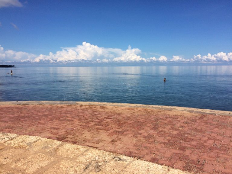 Calm blue sea beside a paved terrace at Keerimalai with a bather standing in the water
