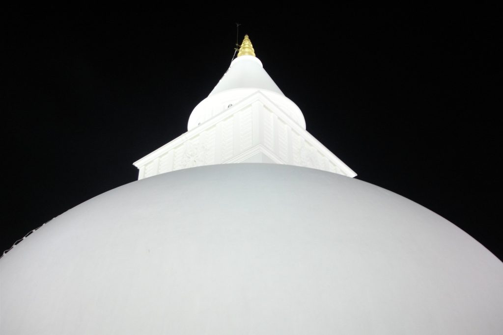 Looking up at the white dome, square harmika with a carved wheel and the gilded finial of Kiri Vehera against the night sky