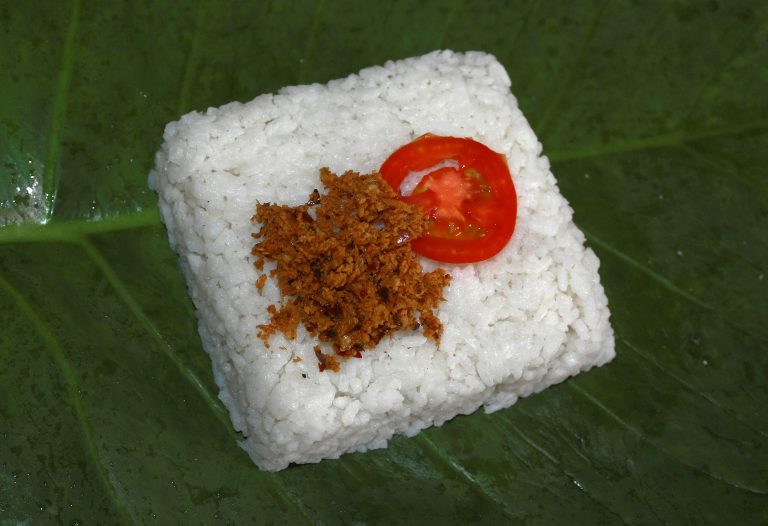 A square of white kiribath, Sri Lankan milk rice, on a banana leaf with a spoonful of red lunumiris chilli sambal