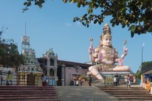 Koneswaram Temple on Swami Rock, with a large seated statue of Shiva beside the temple's carved and painted towers and a flight of steps