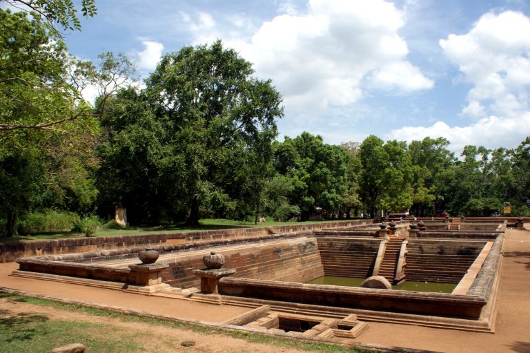 A cut-stone bathing pond with stepped sides and carved stone pots on its rim, surrounded by trees