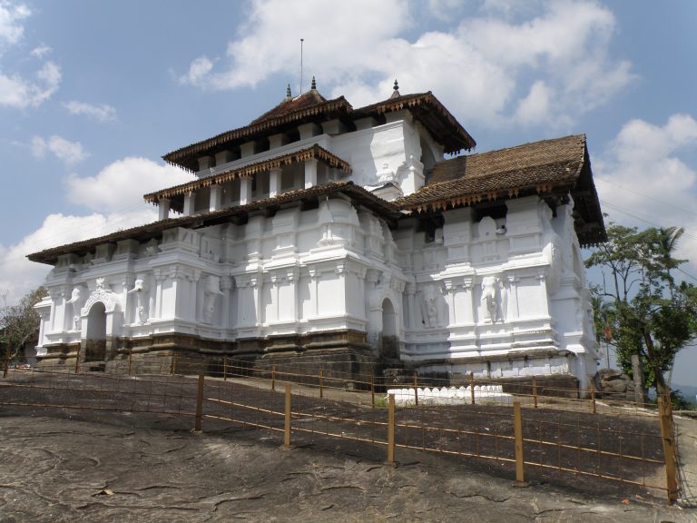 The white, multi-tiered Lankatilaka image house with tiled roofs and elephant figures on its walls, standing on bare rock