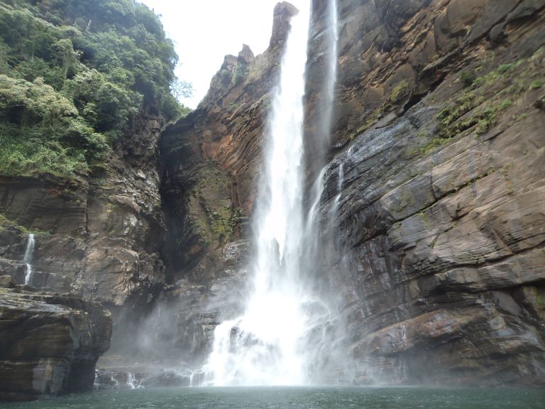 Laxapana Falls in cloud, a thin white stream falling down a cliff above rocks and thick green vegetation