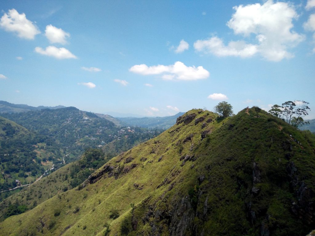 The grassy, rocky ridge of Little Adam's Peak with walkers near the top and Ella town in the valley below