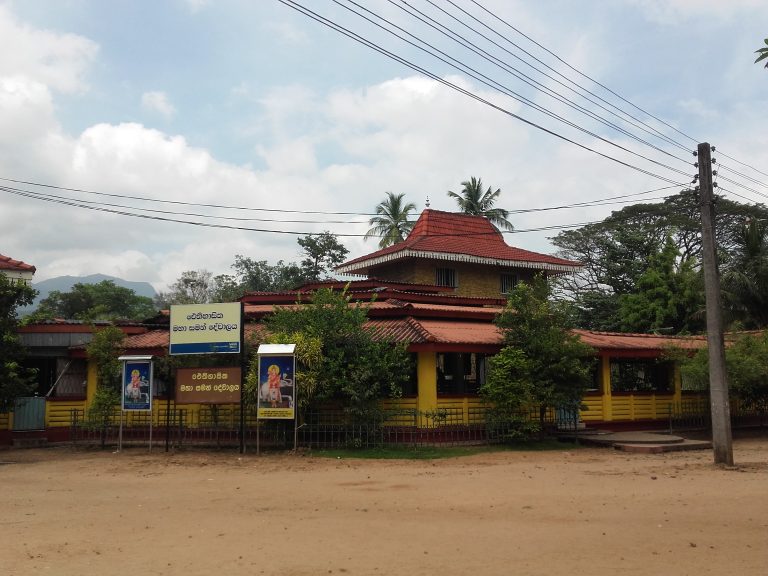 The Maha Saman Devalaya at Mahiyangana, a yellow building with red tiled roofs and Sinhala name boards, with hills behind
