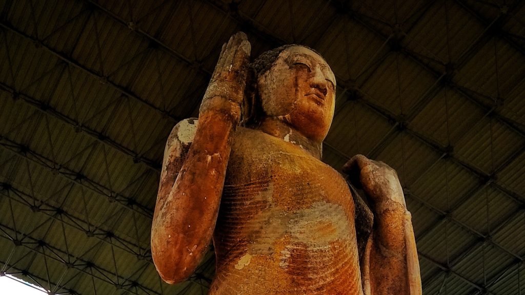 The head and raised right hand of the Maligawila standing Buddha, seen from below under its large metal roof