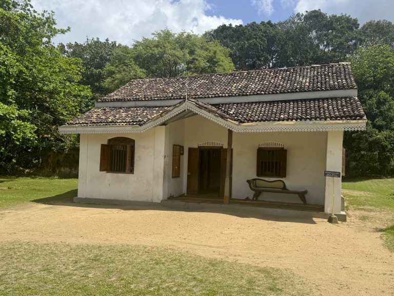 Martin Wickramasinghe's whitewashed ancestral house in Koggala, with a tiled roof, carved white eaves trim, wooden shutters and an old bench on the veranda