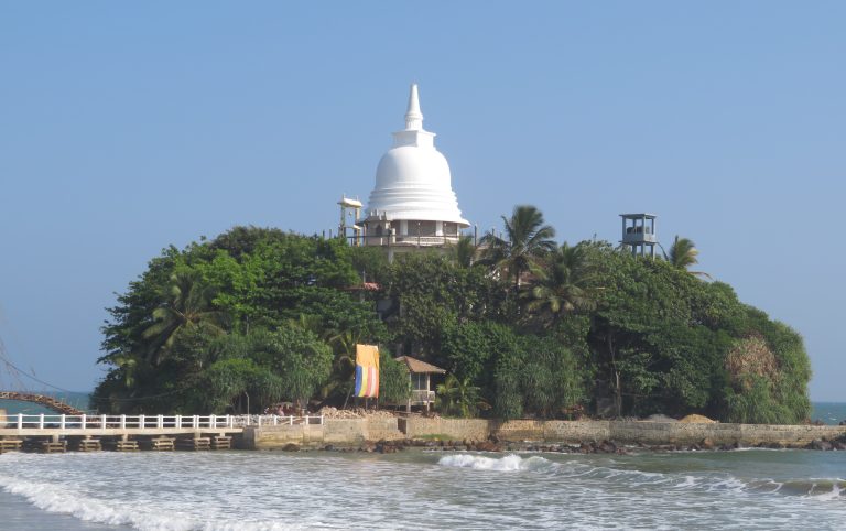 Paravi Duwa, a small tree-covered island off Matara beach with a white stupa on top, linked to the shore by a footbridge