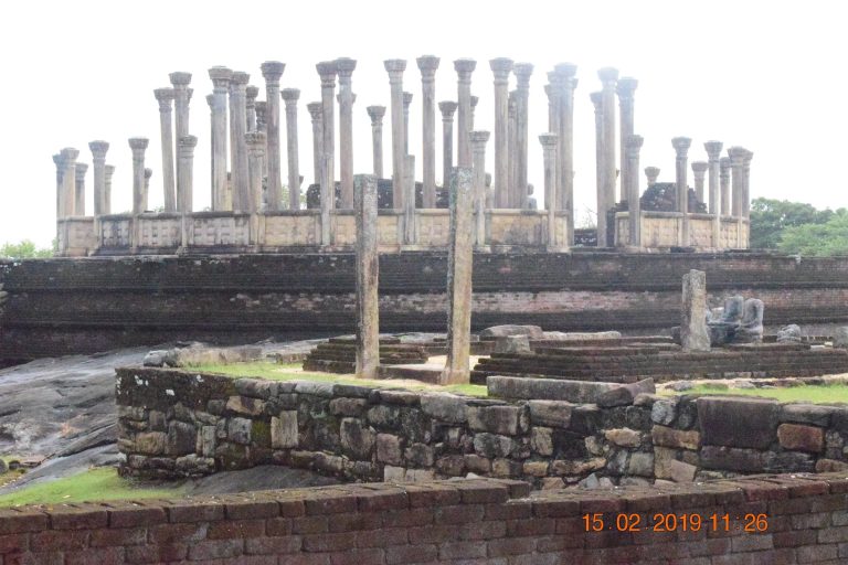 Rings of stone pillars standing on the raised platform of Medirigiriya Vatadage, with a brick base and ruined statues in front