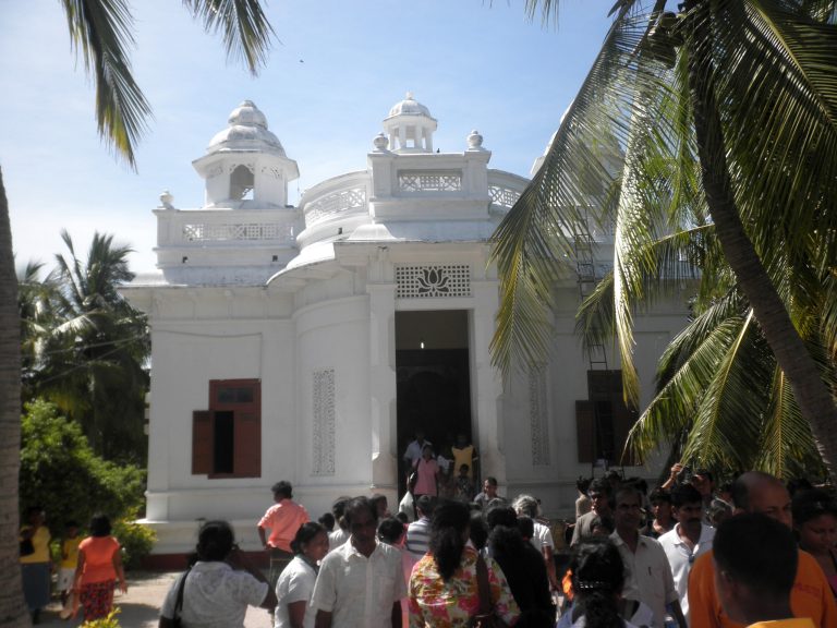 The white image house of Nagadeepa Purana Viharaya with small domed turrets, pilgrims gathered at its door under coconut palms