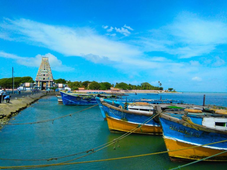 The tall painted eastern gopuram of Nagapooshani Amman Temple at the end of the Nainativu jetty, with blue wooden boats moored in front