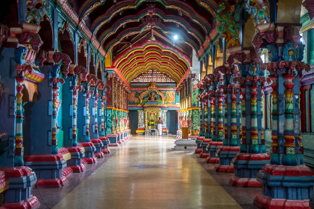 A long temple corridor with painted pillars and layered coloured arches leading to a shrine at the far end
