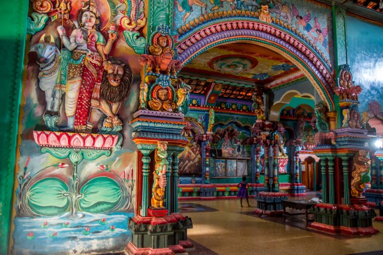 Painted figures of Shiva and a bull on a wall beside colourful carved pillars and an arch inside the temple